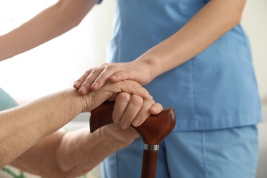 Photo of Nurse assisting elderly woman with cane, closeup