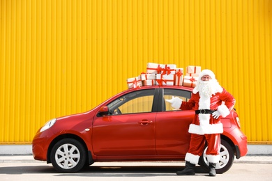 Authentic Santa Claus near red car with gift boxes, outdoors