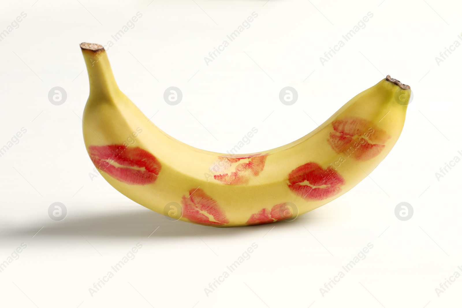 Photo of Banana covered with red lipstick marks on white wooden table. Potency concept