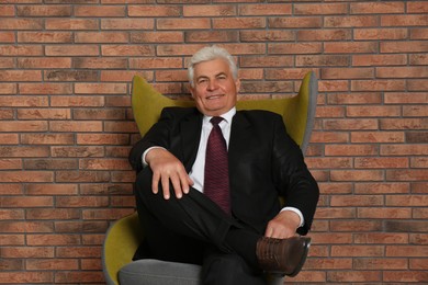 Photo of Happy mature businessman sitting in armchair near brick wall