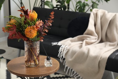 Photo of Vase with bouquet of beautiful leucospermum flowers and air freshener on side table near black sofa in room, space for text