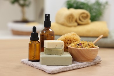 Photo of Bottles of essential oils, bowl with dry flowers, soap bars and natural sponge on light wooden table. Spa therapy