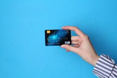 Photo of Woman holding credit card on light blue background, closeup