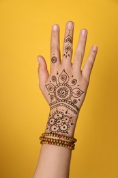 Photo of Woman with beautiful henna tattoo on hand against yellow background, closeup. Traditional mehndi