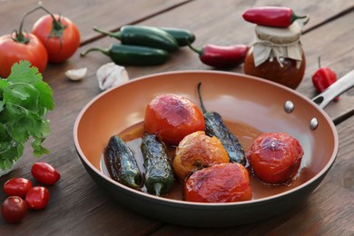 Photo of Frying pan with ingredients for salsa sauce on wooden table