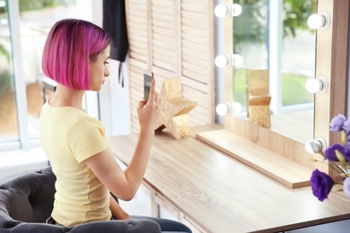 Photo of Young woman with color hair taking selfie in front of mirror in beauty salon. Modern trend