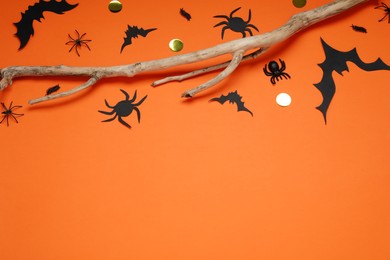 Flat lay composition with paper bats, spiders and wooden branch on orange background, space for text. Halloween decor