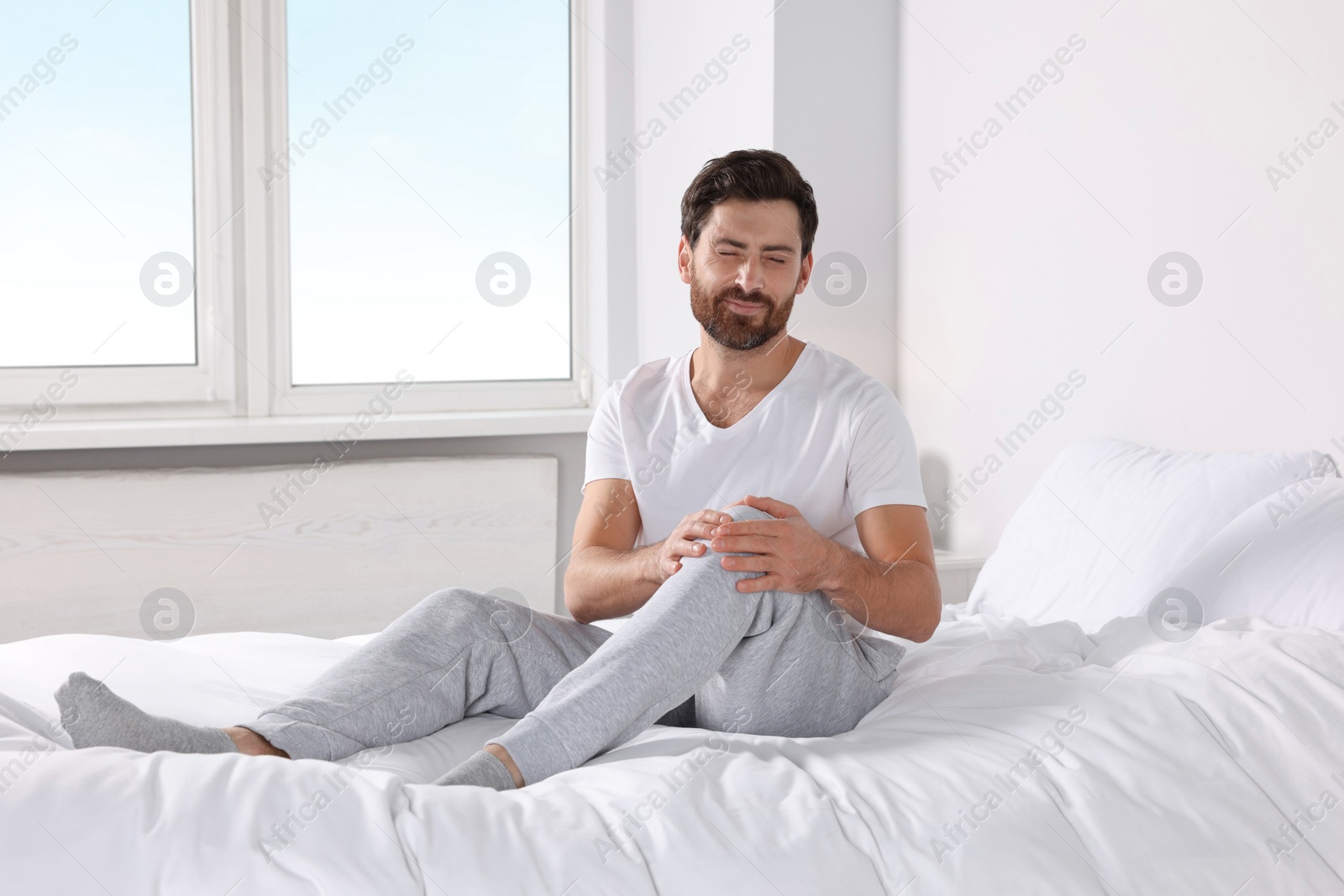 Photo of Man suffering from leg pain on bed at home