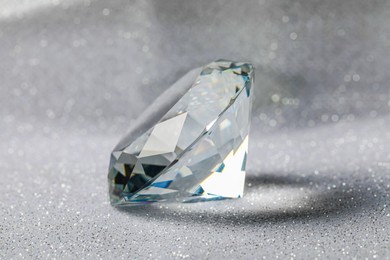 Photo of Beautiful dazzling diamond on shiny glitter background, closeup. Precious gemstone