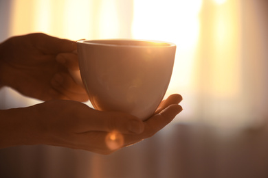 Photo of Woman holding cup of drink on blurred background, closeup. Lazy morning