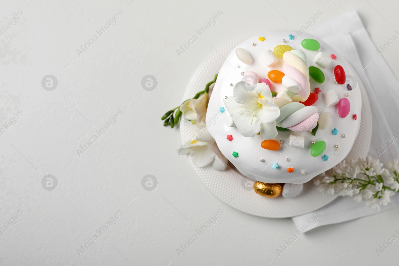 Photo of Traditional Easter cake with sprinkles, jelly beans, marshmallows and decorated eggs on white table, flat lay. Space for text