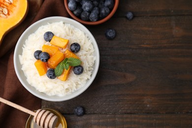 Photo of Bowl of delicious rice porridge with blueberries, pumpkin and honey on wooden table, flat lay. Space for text