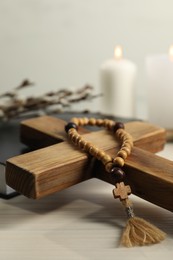 Wooden cross and rosary beads on white table, closeup