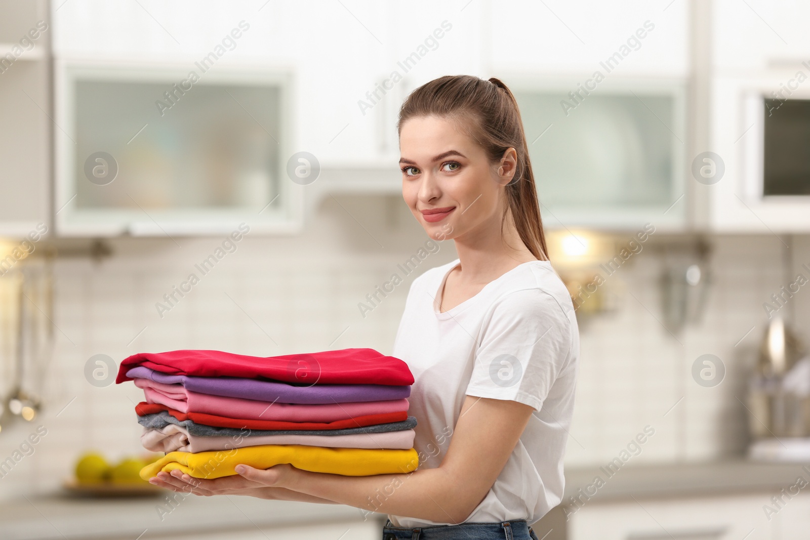 Photo of Woman holding folded clean clothes in kitchen. Laundry day