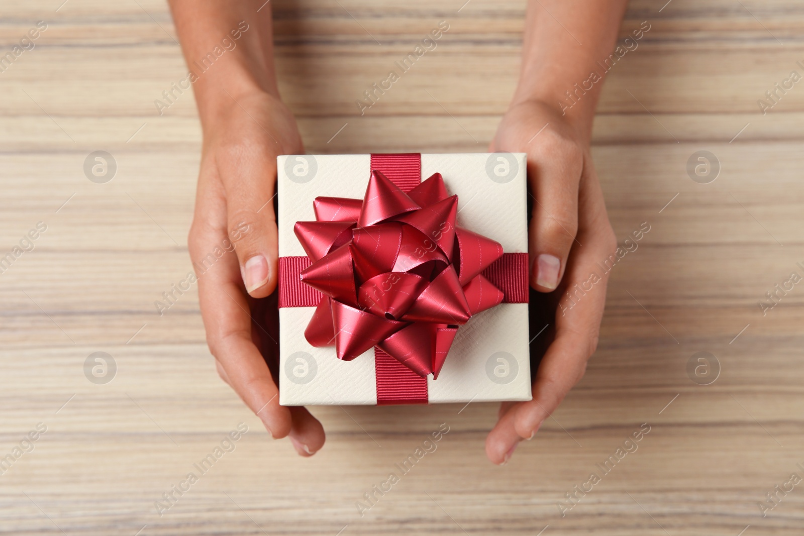 Photo of Woman holding beautiful gift box over wooden table, top view