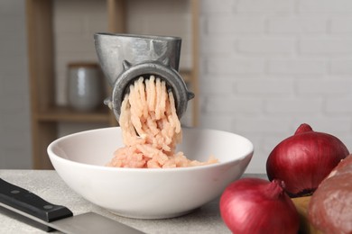 Metal meat grinder with chicken mince and products on light grey table indoors