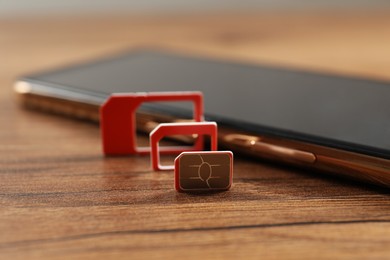 Red multi SIM card and mobile phone on wooden table, closeup