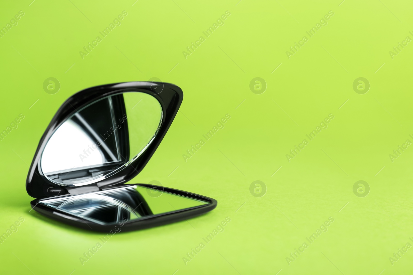 Photo of Stylish cosmetic pocket mirror on light green background. Space for text