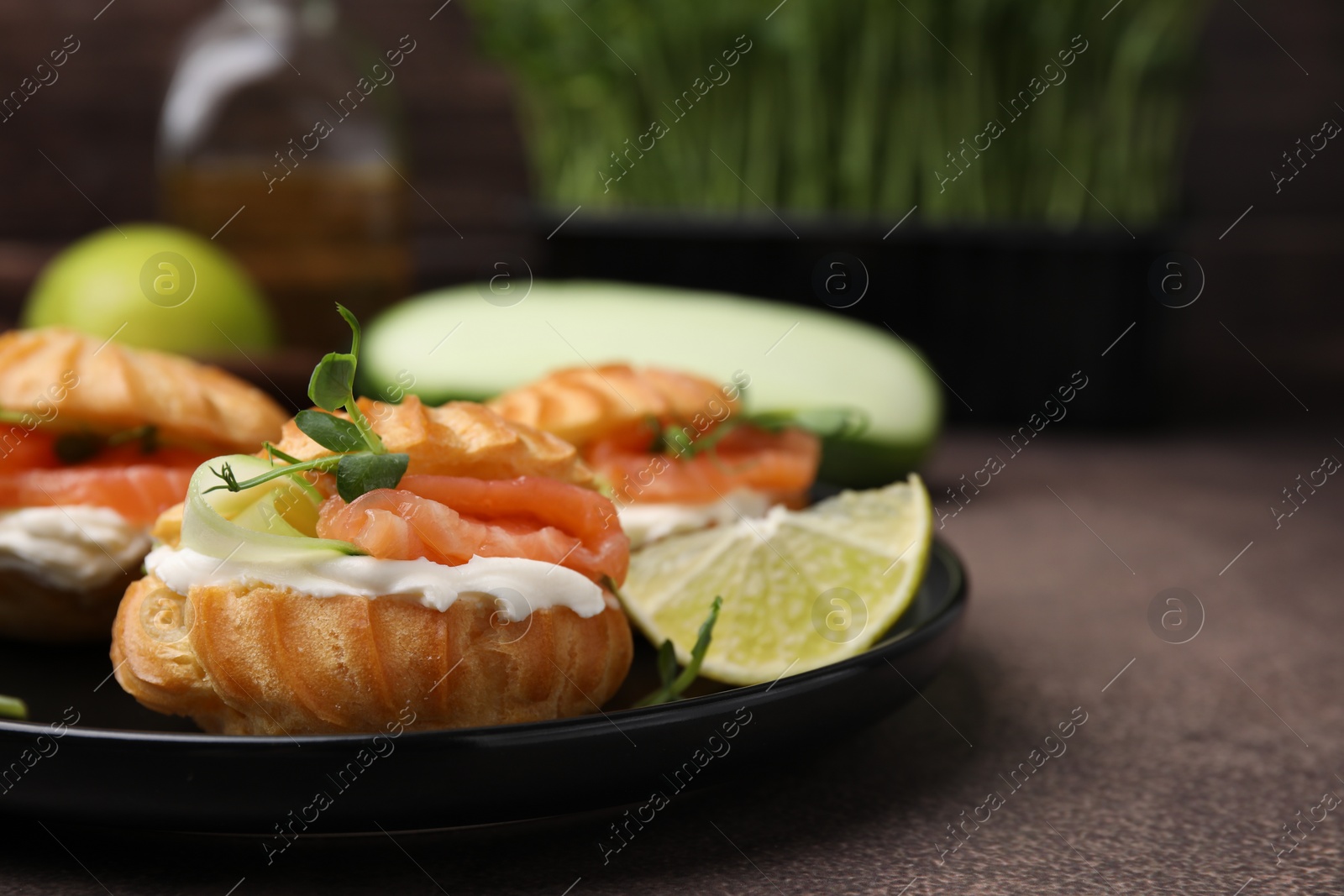 Photo of Delicious profiteroles with cream cheese, salmon and cucumber on textured table, closeup. Space for text