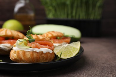 Photo of Delicious profiteroles with cream cheese, salmon and cucumber on textured table, closeup. Space for text