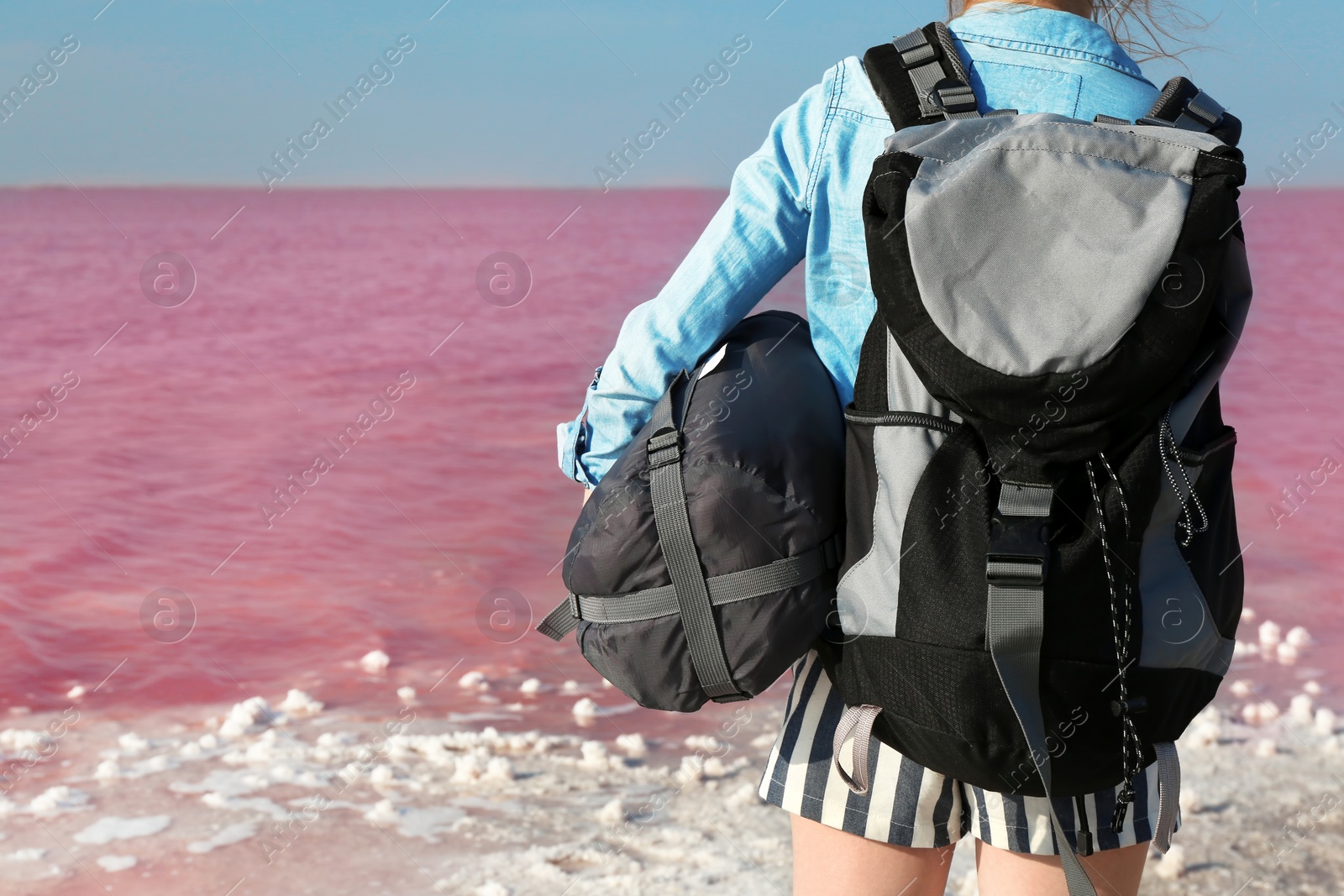 Photo of Woman with backpack and sleeping bag on coast of pink lake