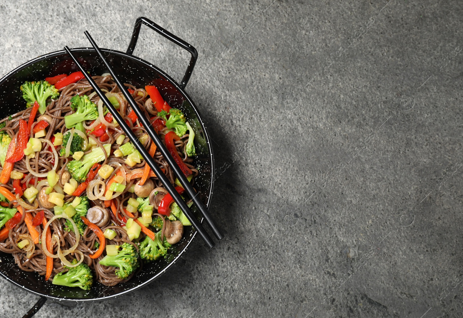 Photo of Stir fried noodles with mushrooms and vegetables in wok on grey table, top view. Space for text