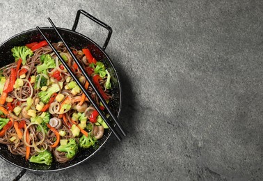 Stir fried noodles with mushrooms and vegetables in wok on grey table, top view. Space for text