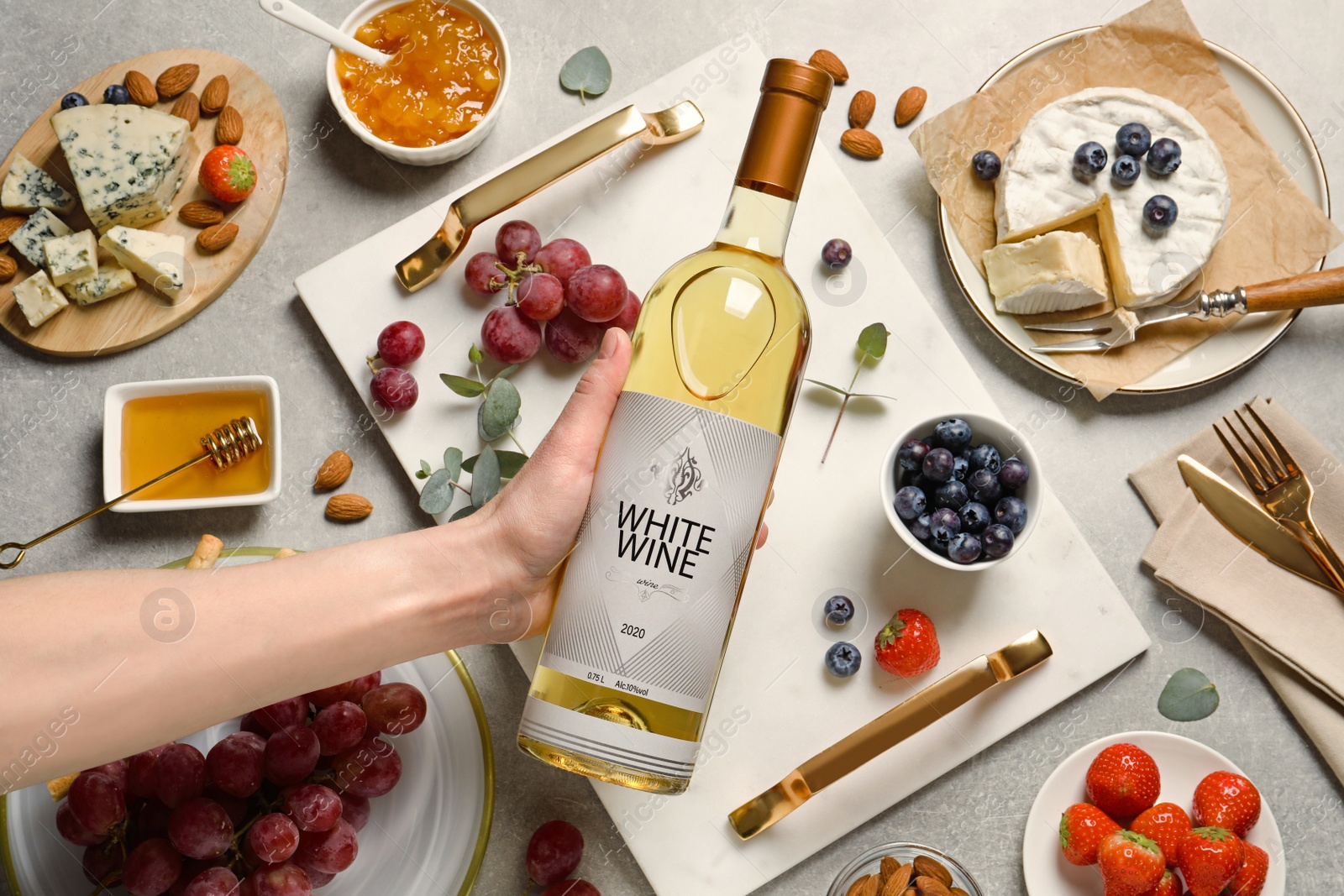 Photo of Woman holding bottle of white wine at grey table with snacks, top view