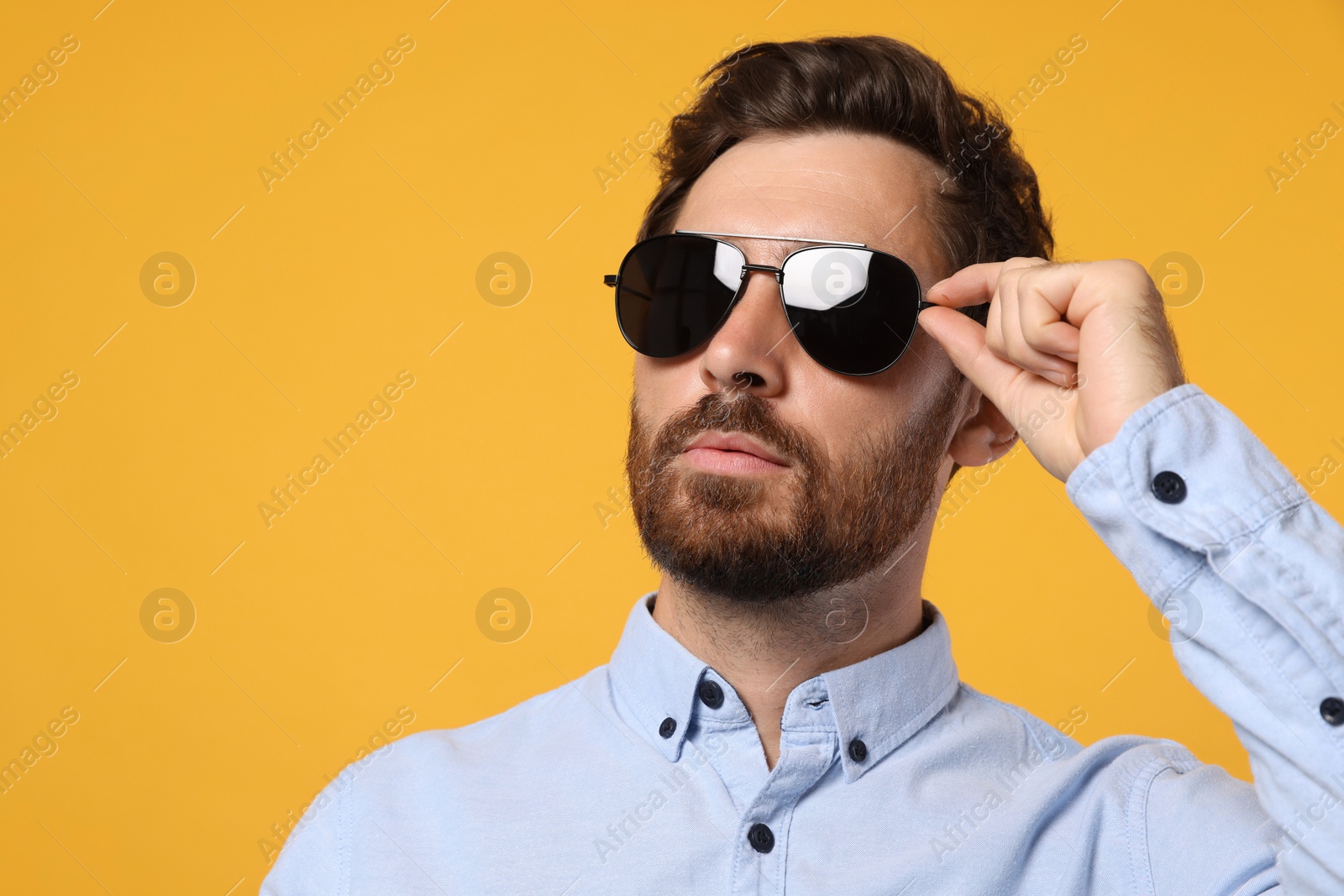 Photo of Portrait of bearded man with stylish sunglasses on orange background. Space for text