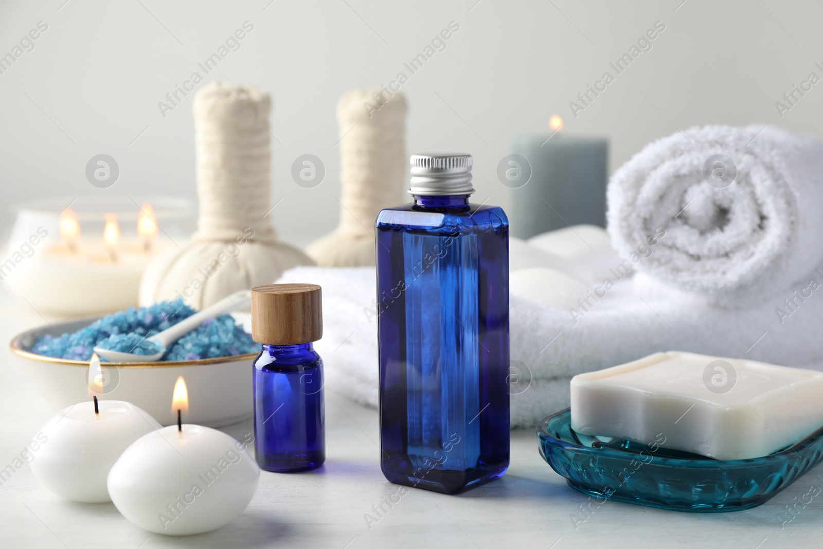 Photo of Spa composition. Cosmetic products, soap, towels, sea salt and burning candles on light table