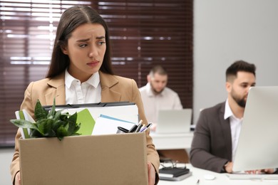 Upset dismissed woman carrying box with personal stuff in office