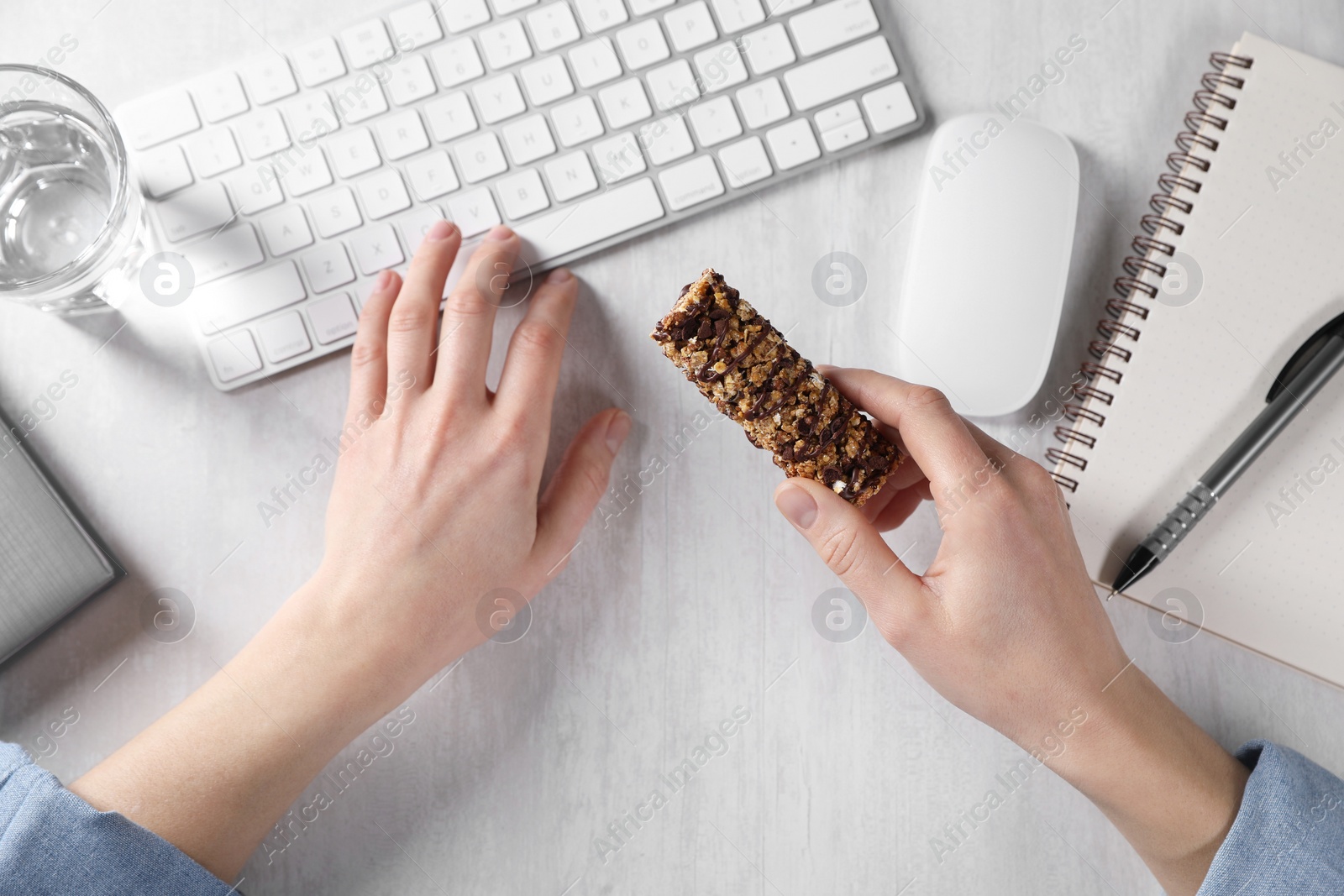 Photo of Woman holding tasty granola bar working with computer at light table, top view