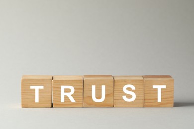 Photo of Word Trust made of wooden cubes on grey background, space for text