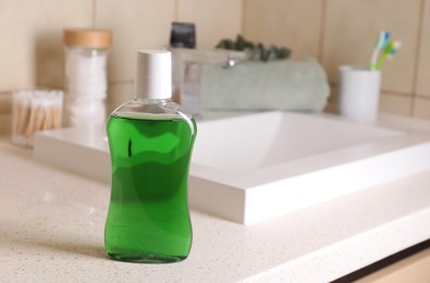 Photo of Fresh mouthwash in bottle on countertop in bathroom. Space for text