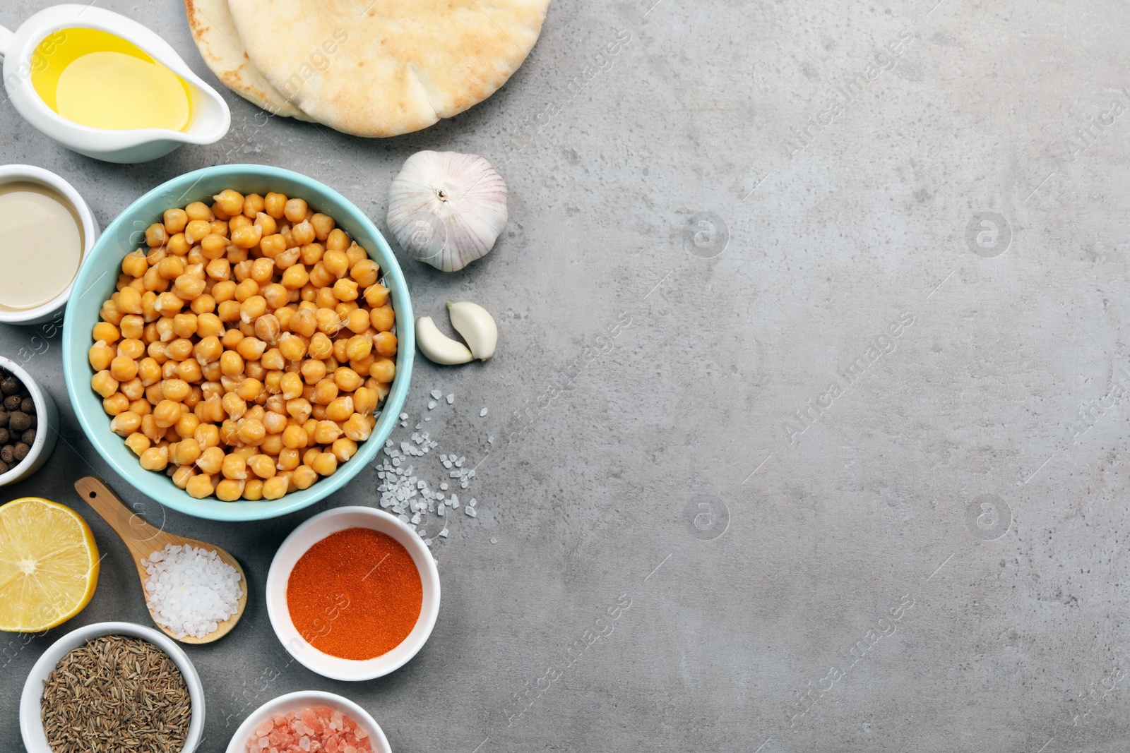 Photo of Delicious chickpeas and different ingredients on light grey table, flat lay with space for text. Cooking hummus