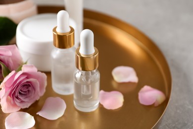 Photo of Bottles of cosmetic serum, beauty products and flowers on table, closeup