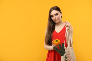 Photo of Woman with string bag of fresh vegetables on orange background, space for text
