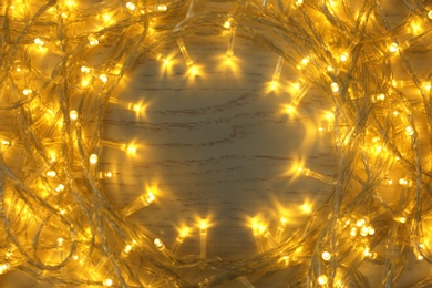 Photo of Frame made of glowing Christmas lights on white wooden background, top view. Space for text