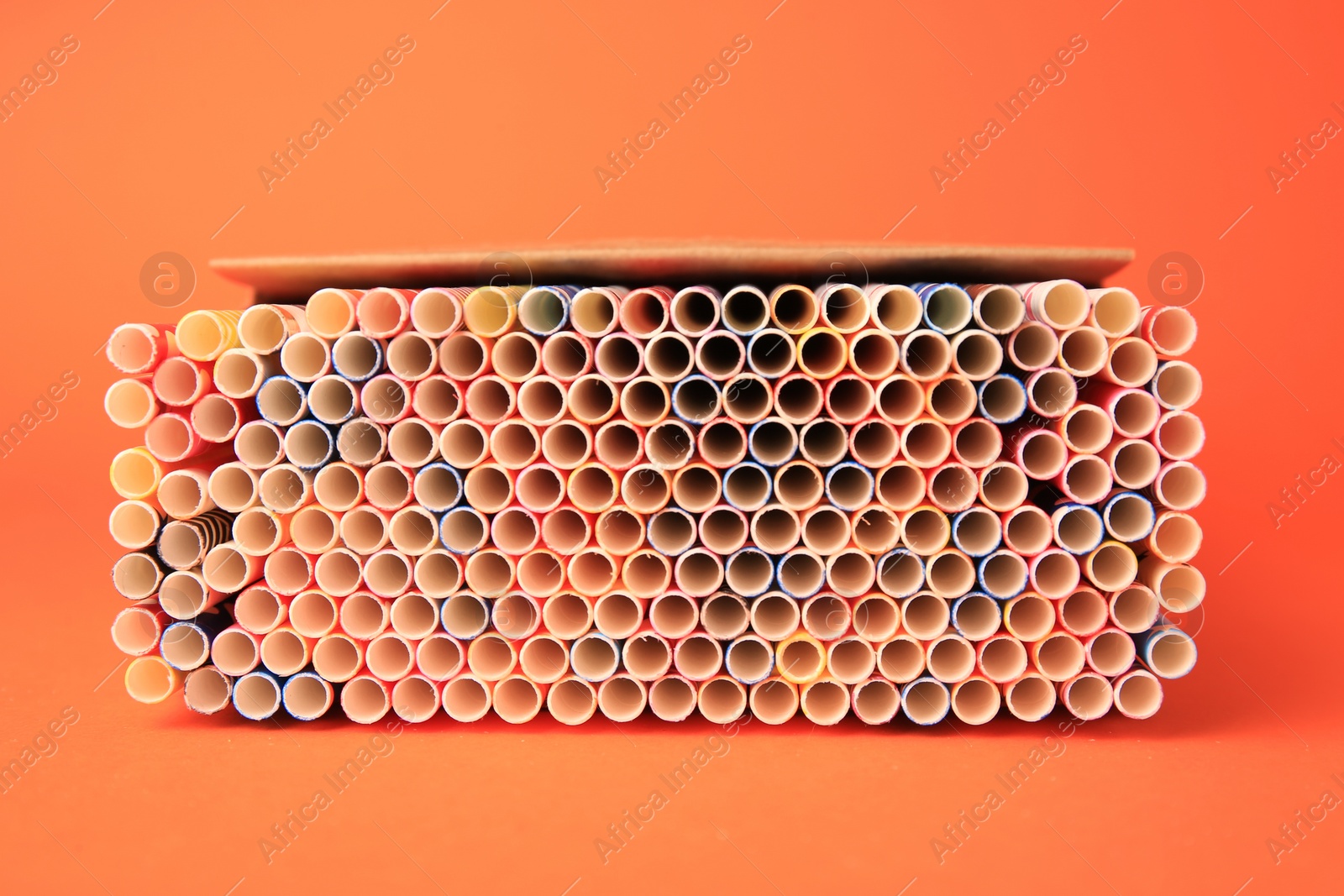 Photo of Box with many paper drinking straws on orange background