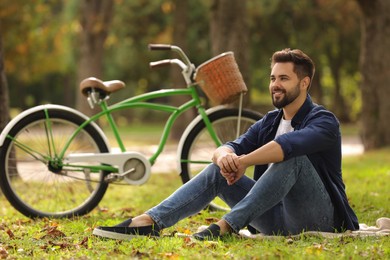 Young man sitting on green grass near bicycle in park