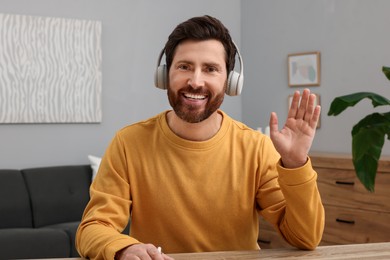 Photo of Man in headphones greeting someone at wooden table indoors
