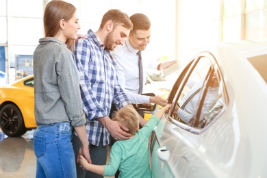 Young family choosing new car with salesman in salon