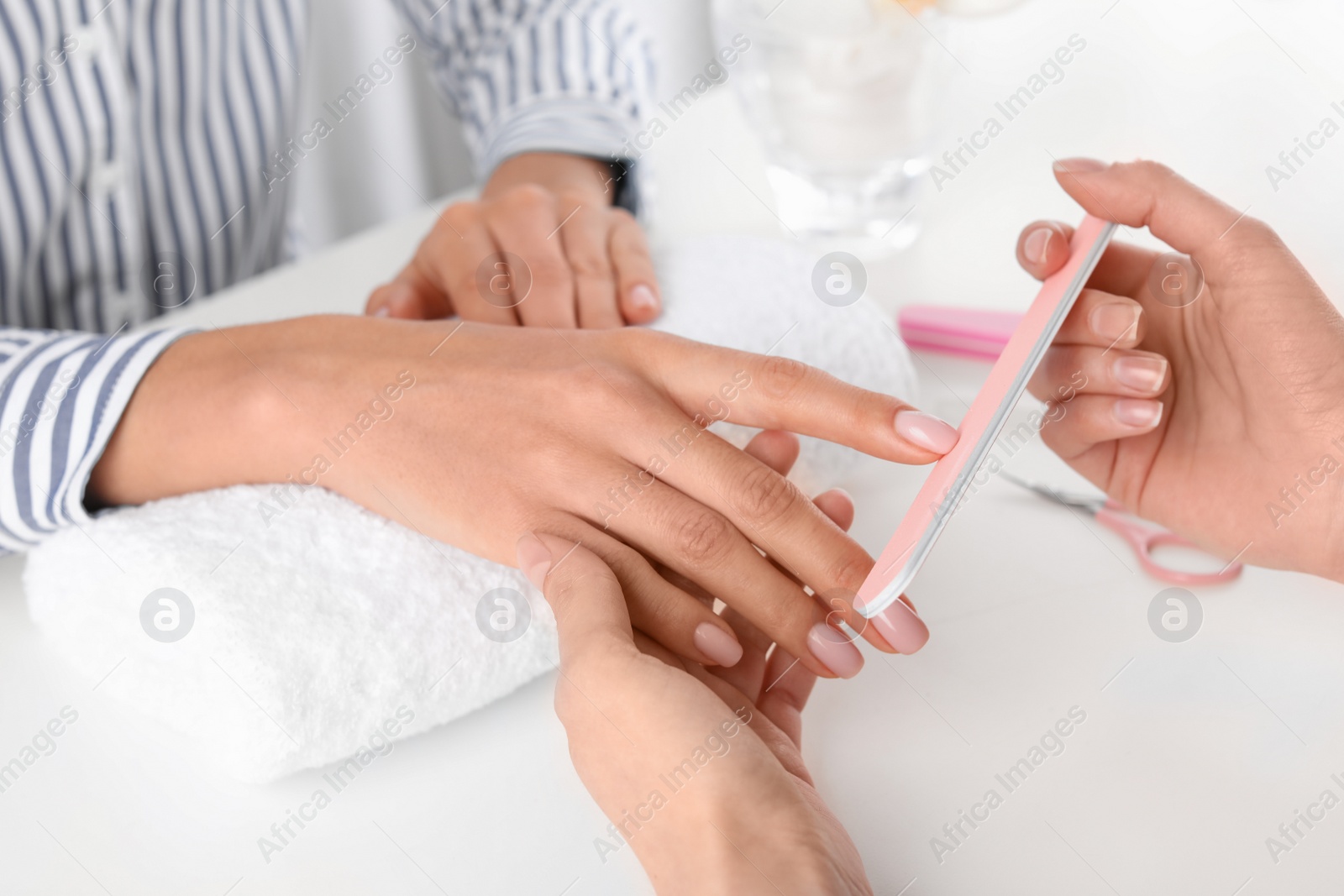 Photo of Manicurist filing client's nails covered with polish in salon, closeup