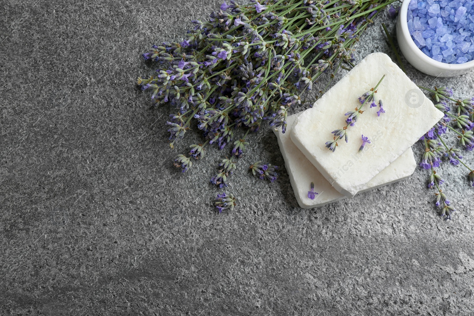 Photo of Hand made soap bars with lavender flowers on grey stone table, flat lay. Space for text