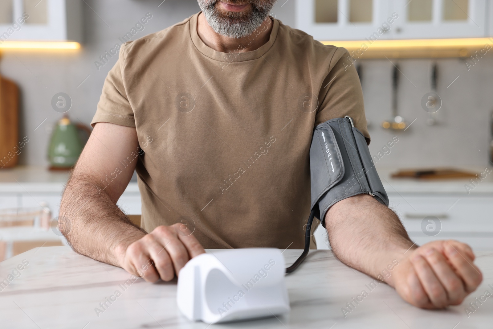 Photo of Man measuring blood pressure at table indoors, closeup