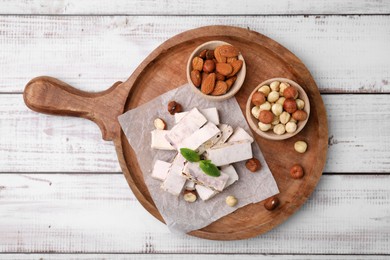 Photo of Pieces of delicious nutty nougat on white wooden table, top view