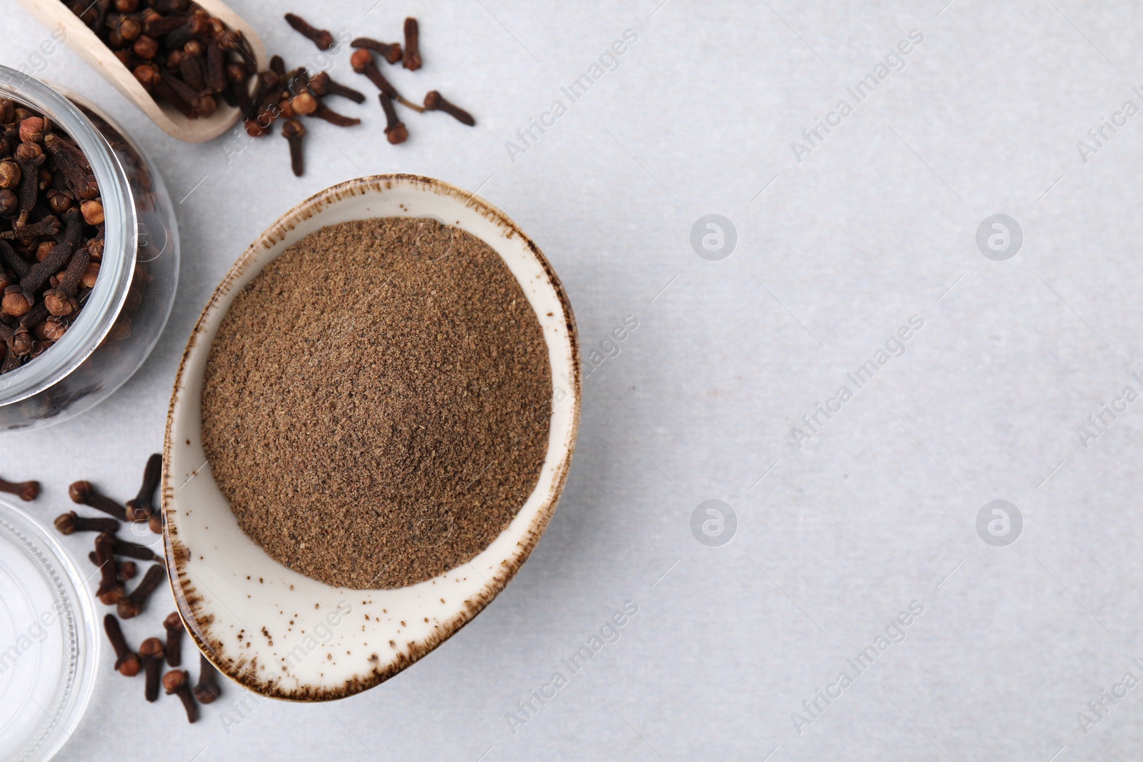 Photo of Aromatic clove powder, scoop and dried buds on light table, flat lay. Space for text