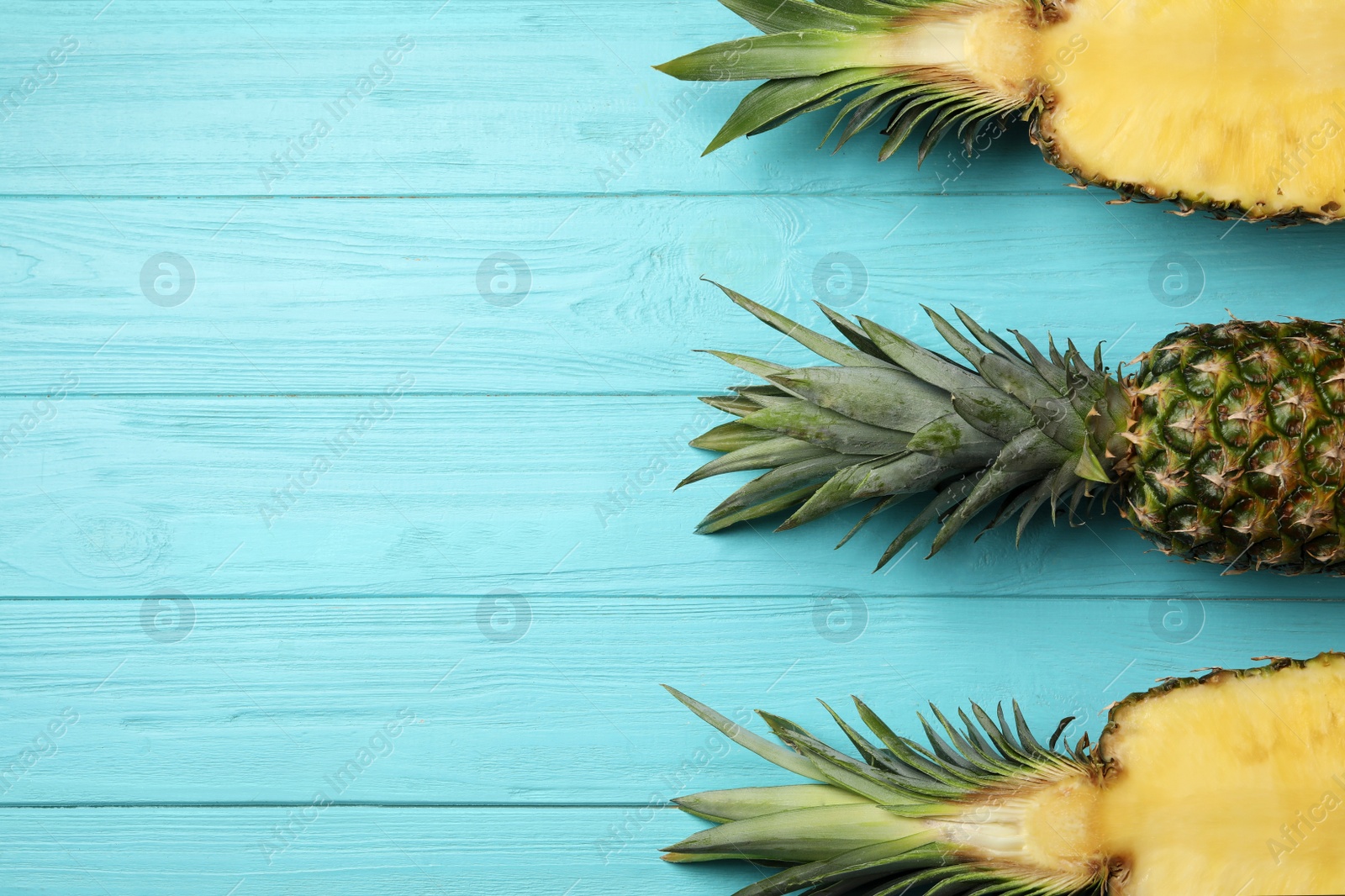 Photo of Fresh whole and cut pineapples on light blue wooden background, top view. Space for text