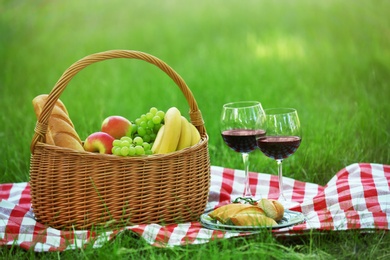 Photo of Wicker basket with food and wine on blanket in park. Summer picnic