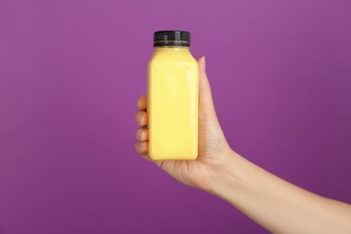 Woman holding bottle with delicious smoothie on color background